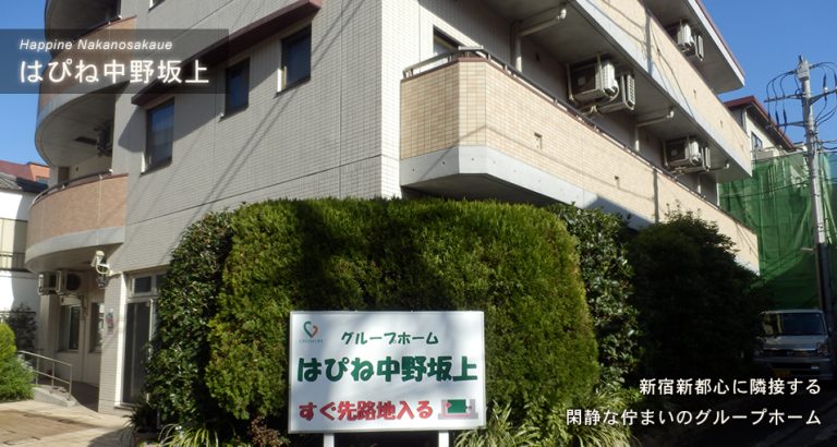 介護施設の建物外観。緑の生垣と施設名看板が見える。